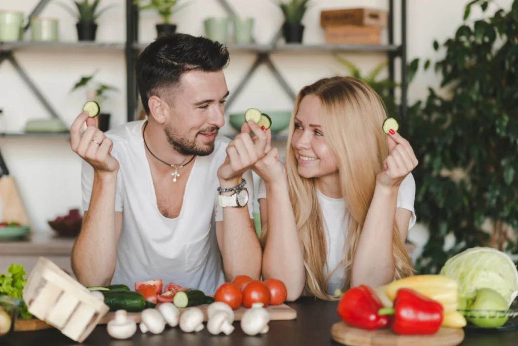 smiling young couple holding cucumber slice looking each other because they love the benefits of a plant based diet