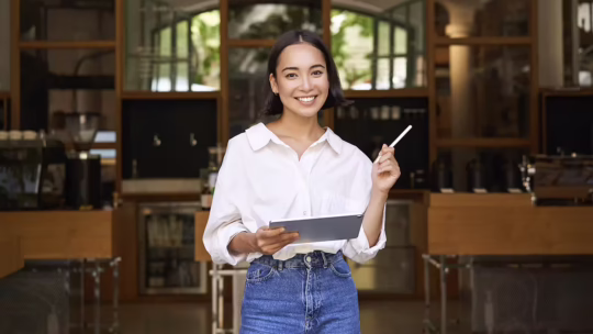 asian woman manager standing with tablet front cafe entrance welcomes guests
